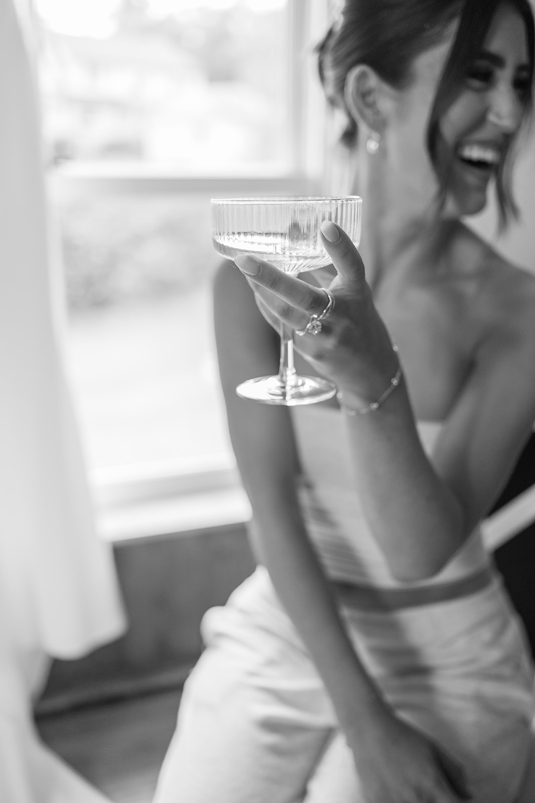Bride laughing with a glass of wine in the window light of The Nest at City Winery Hudson Valley, black and white